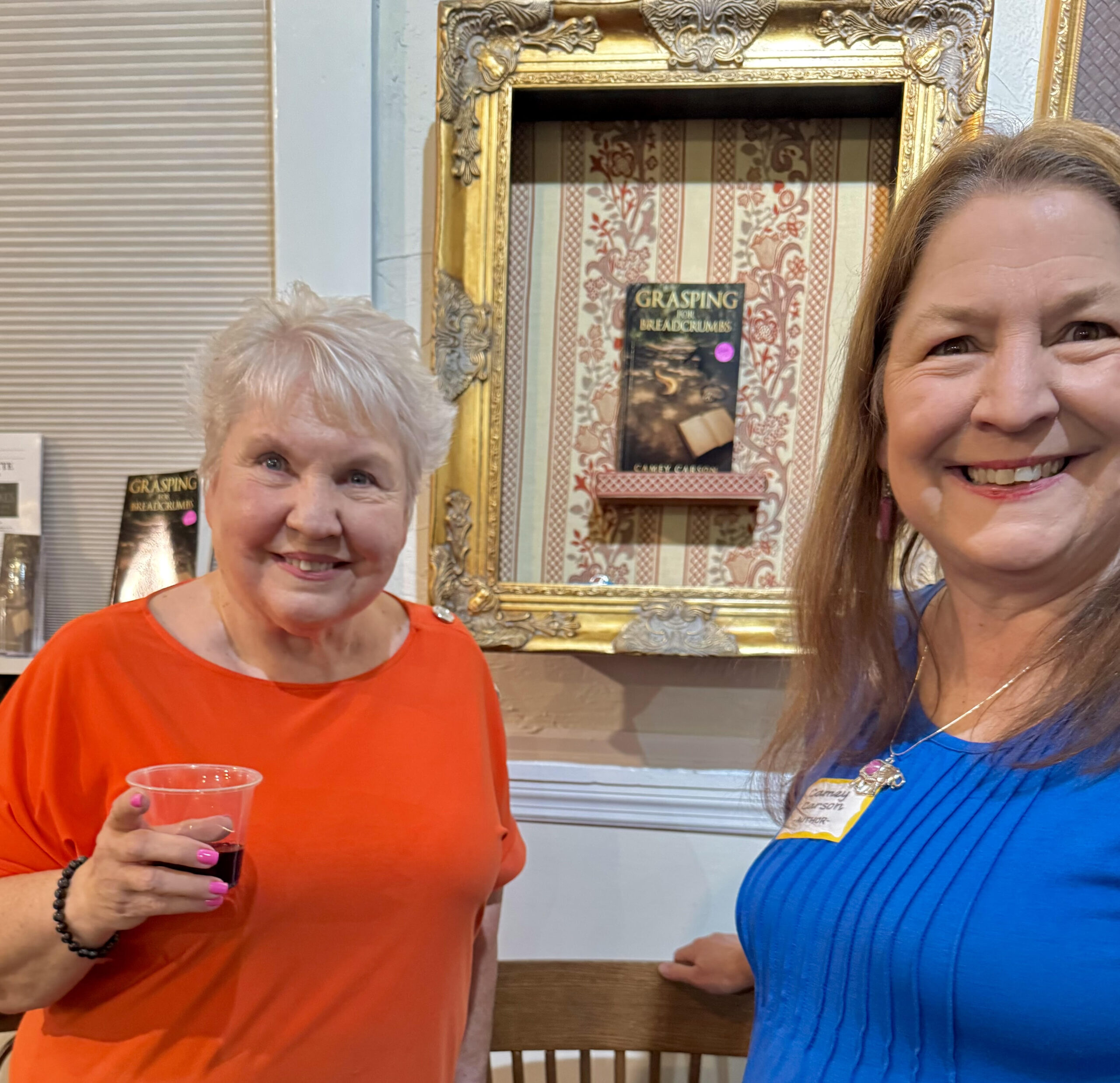 Author Camey Carson pictured with an attendee in front of her framed book, "Grasping for Breadcrumbs."