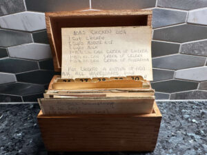 Picture of a wood recipe box with a recipe card balanced on the top with the words: Mom's Chicken Dish - 1 cut chicken, 2 cups minute rice, 2 cups mils, 1 10.5 ox can cream of chicken, 1 10.5 oz can cream of celery, 1 10.5 oz can cream of mushroom. Put chicken in bottom of pan, mix all ingredients.